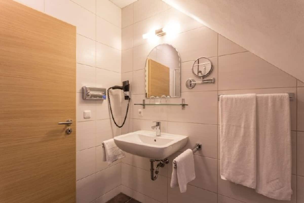 Un baño con lavamanos, espejo, toallero y ducha.