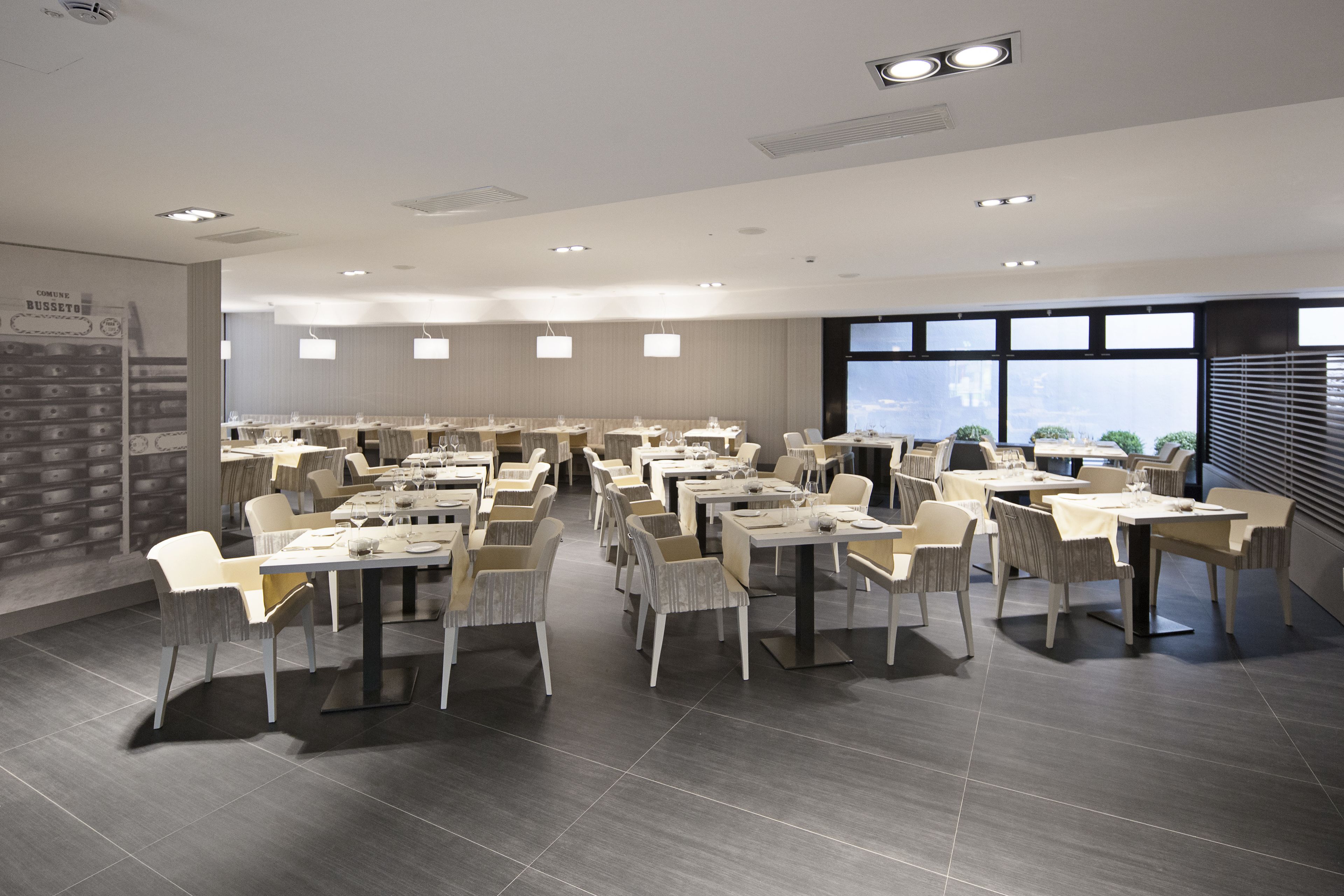 A spacious dining area with multiple tables and chairs, large windows, and a modern ceiling design.