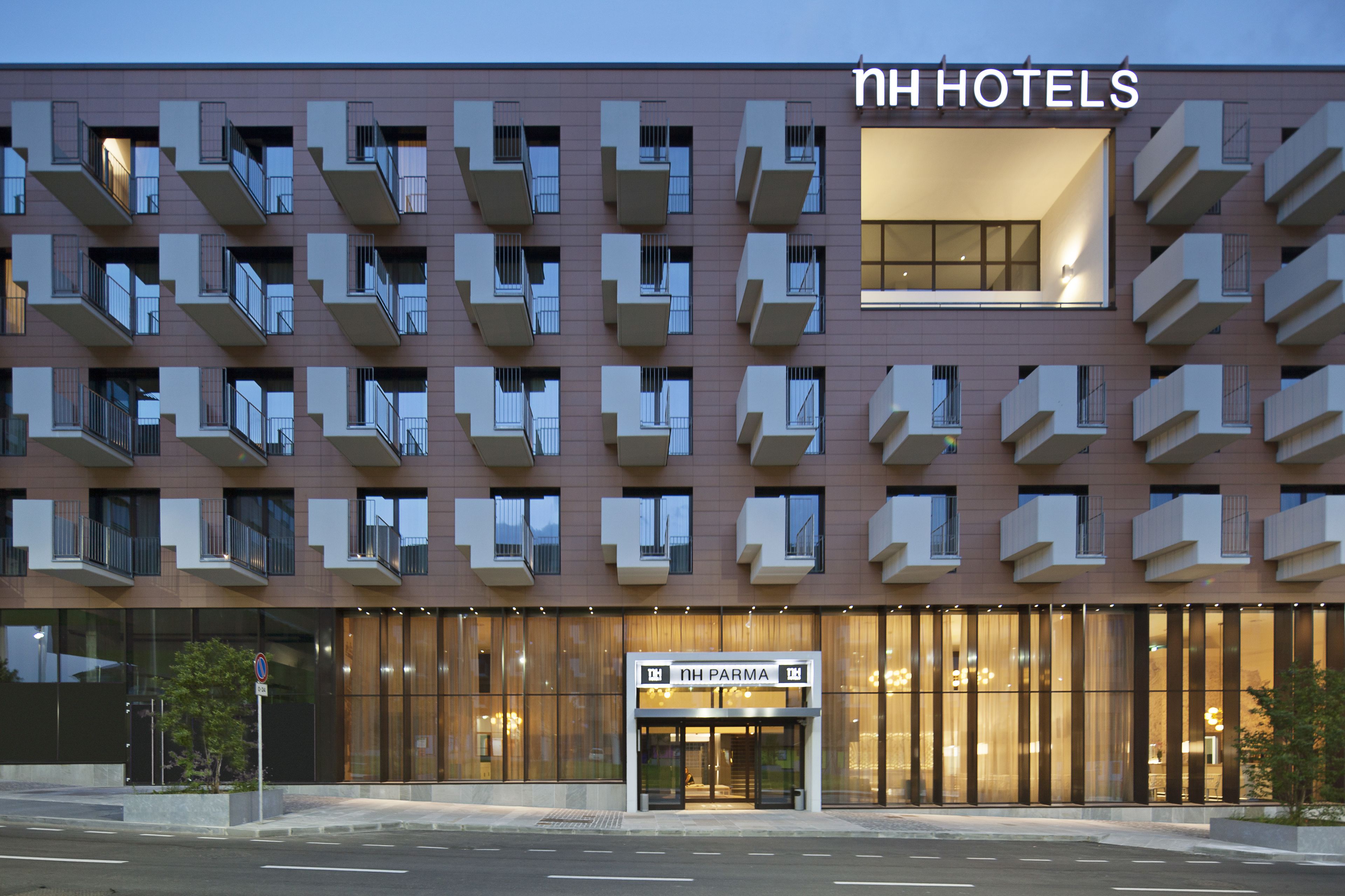 Un hôtel moderne doté de nombreux balcons, d’une entrée imposante et d’une enseigne indiquant « NH PARMA ».