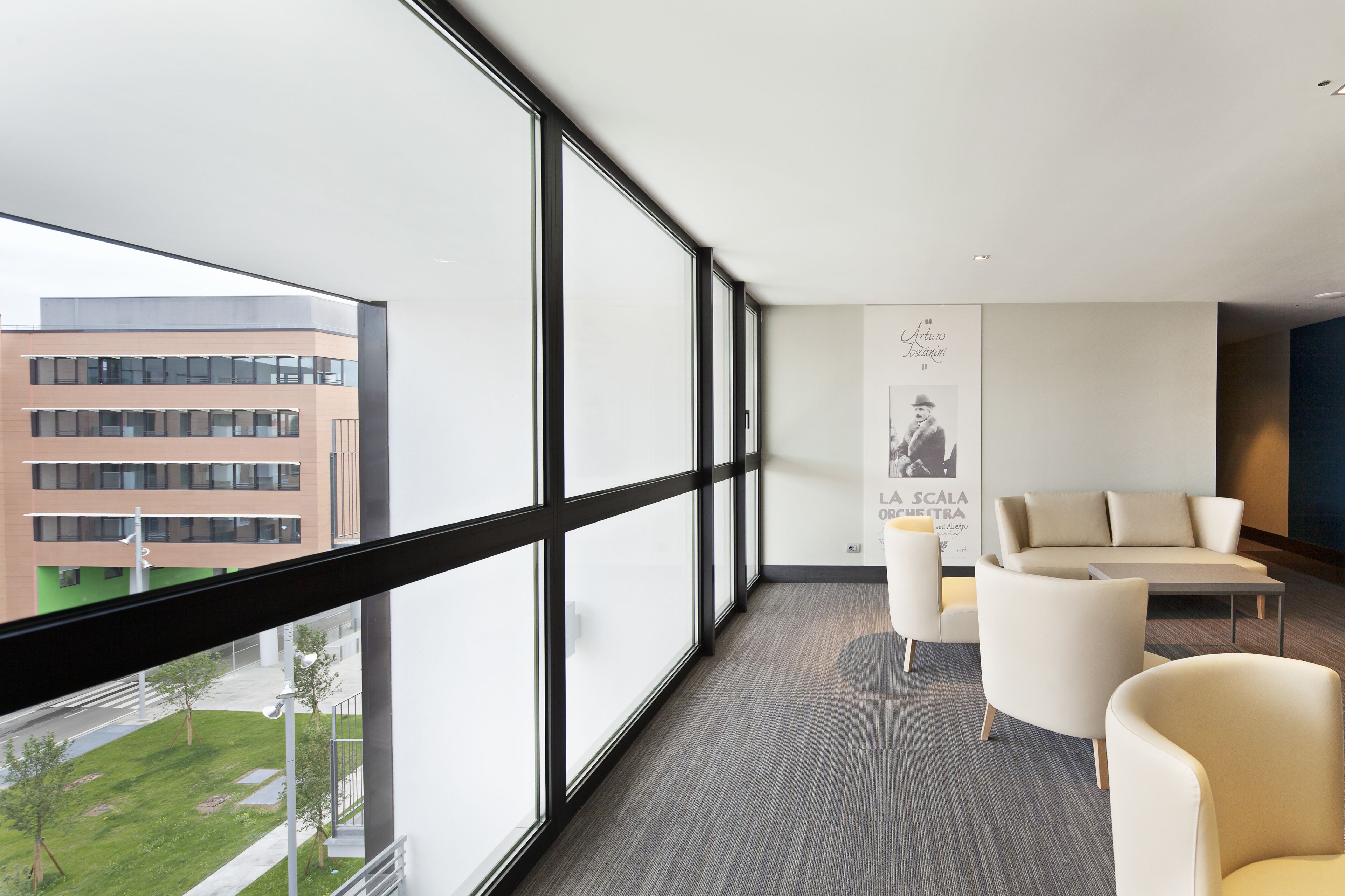 A modern hotel room with large windows, a sofa, and a poster on the wall.