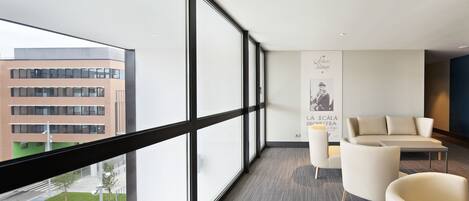 A modern hotel room with large windows, a sofa, and a poster on the wall.