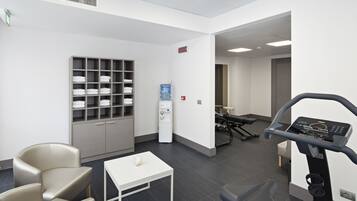 Ein moderner Fitnessraum mit Laufband, Trainingsstühlen, Wasserspender und ordentlich drapierten Handtüchern.