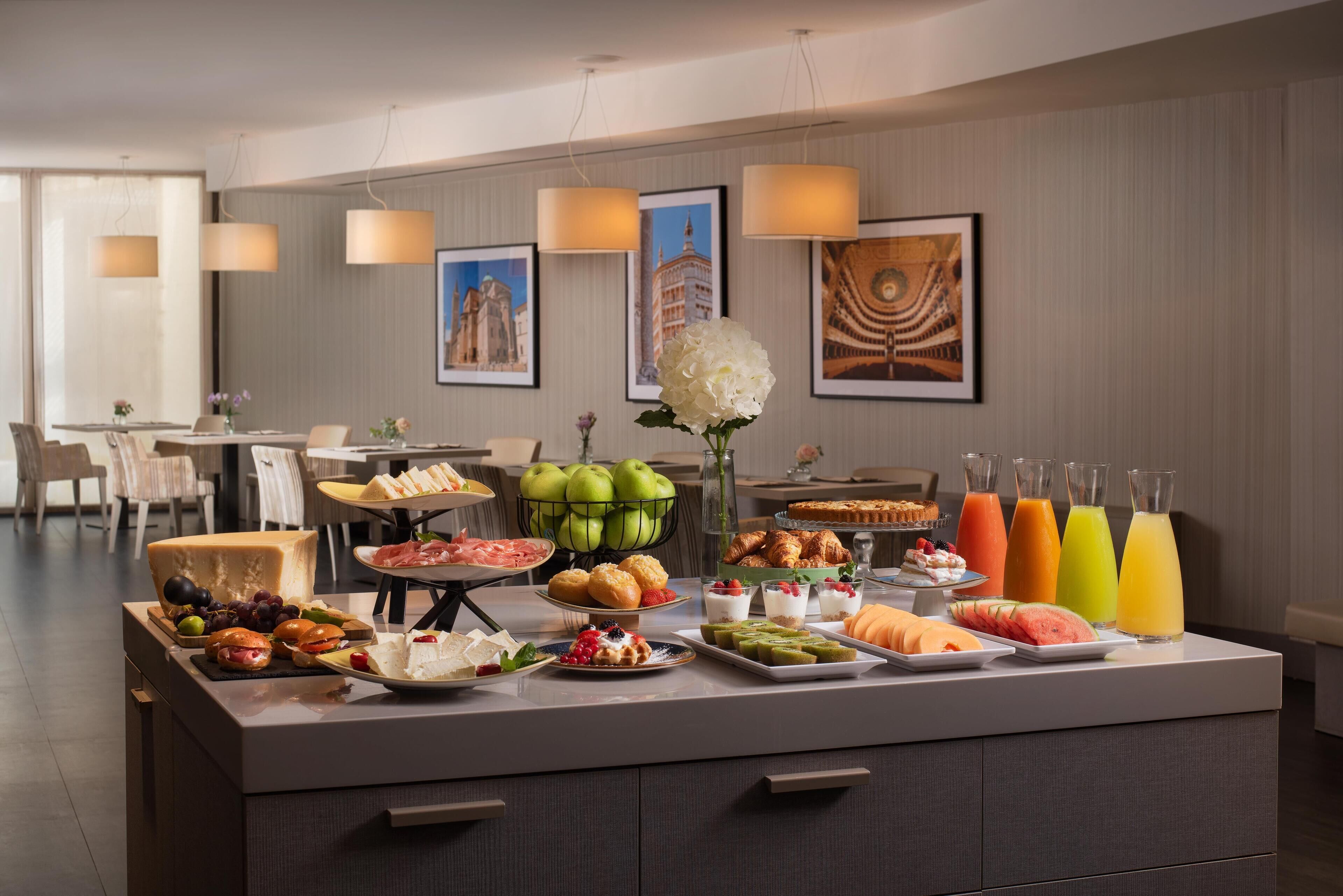 Una mesa de buffet con diversas opciones de comida y bebidas, un florero con flores y cuadros en la pared.