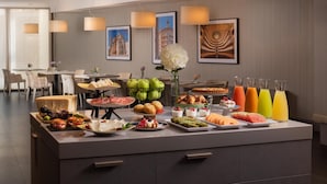 A buffet spread with various food items and drinks, a vase with flowers, and framed pictures on the wall.