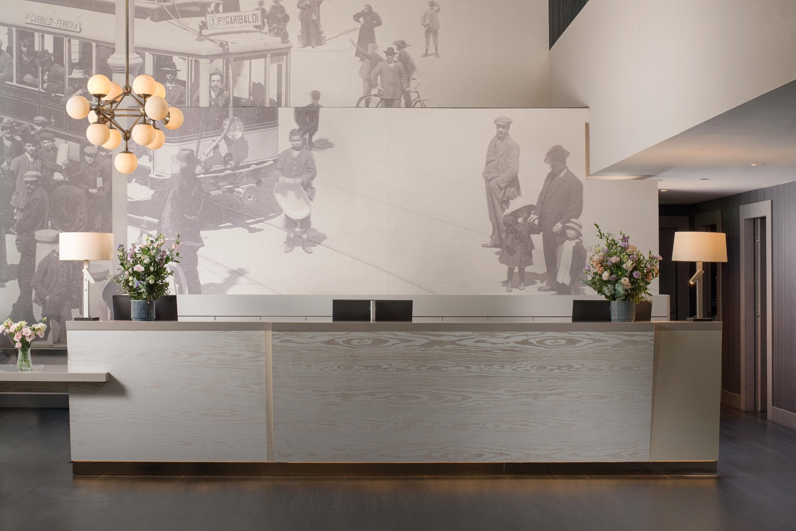 Una reception dal design moderno, con un'ampia parete affrescata raffigurante figure storiche, due piante in vaso e un originale lampadario sferico.