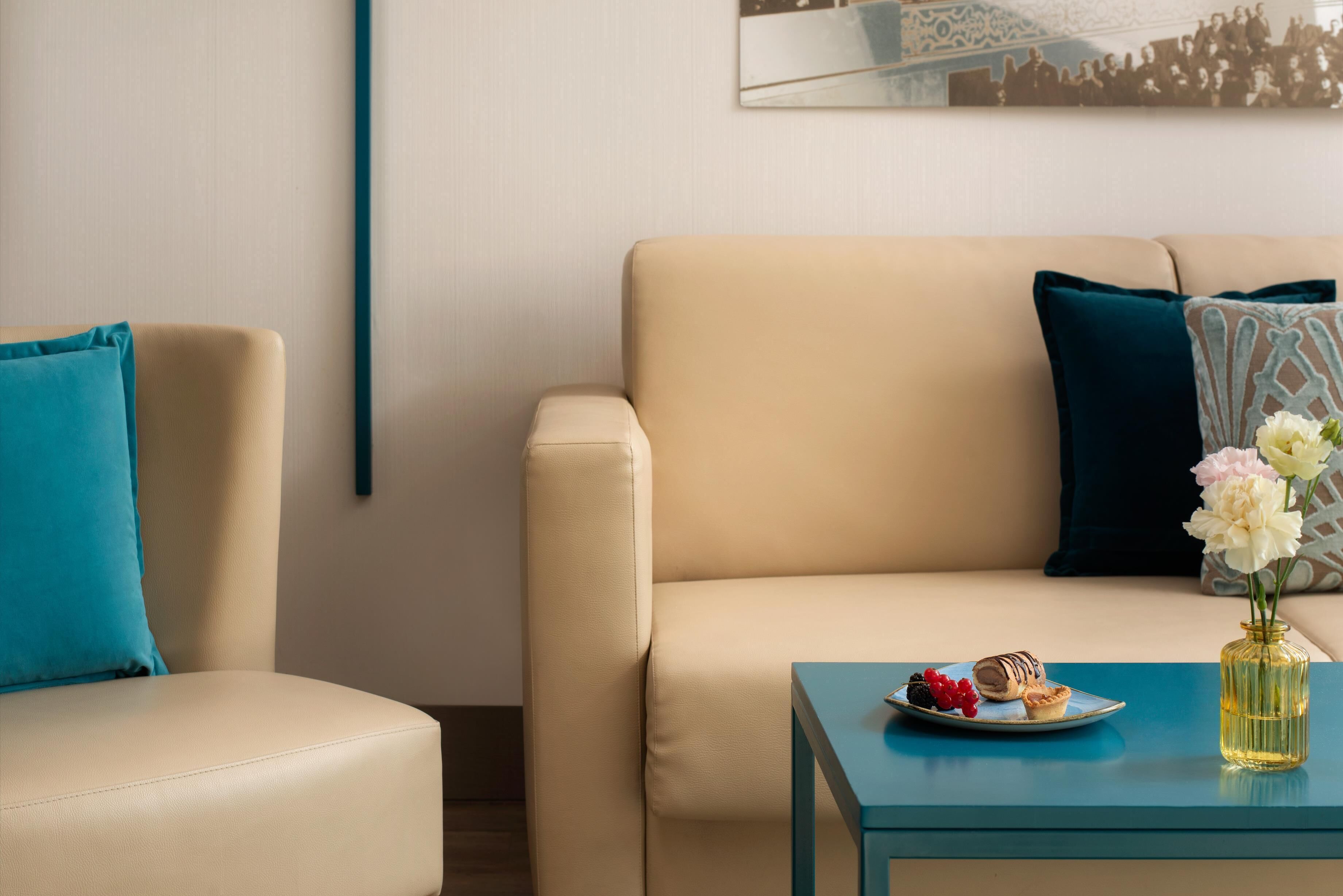A modern living room with a beige sofa, a blue table, and a vase with flowers.