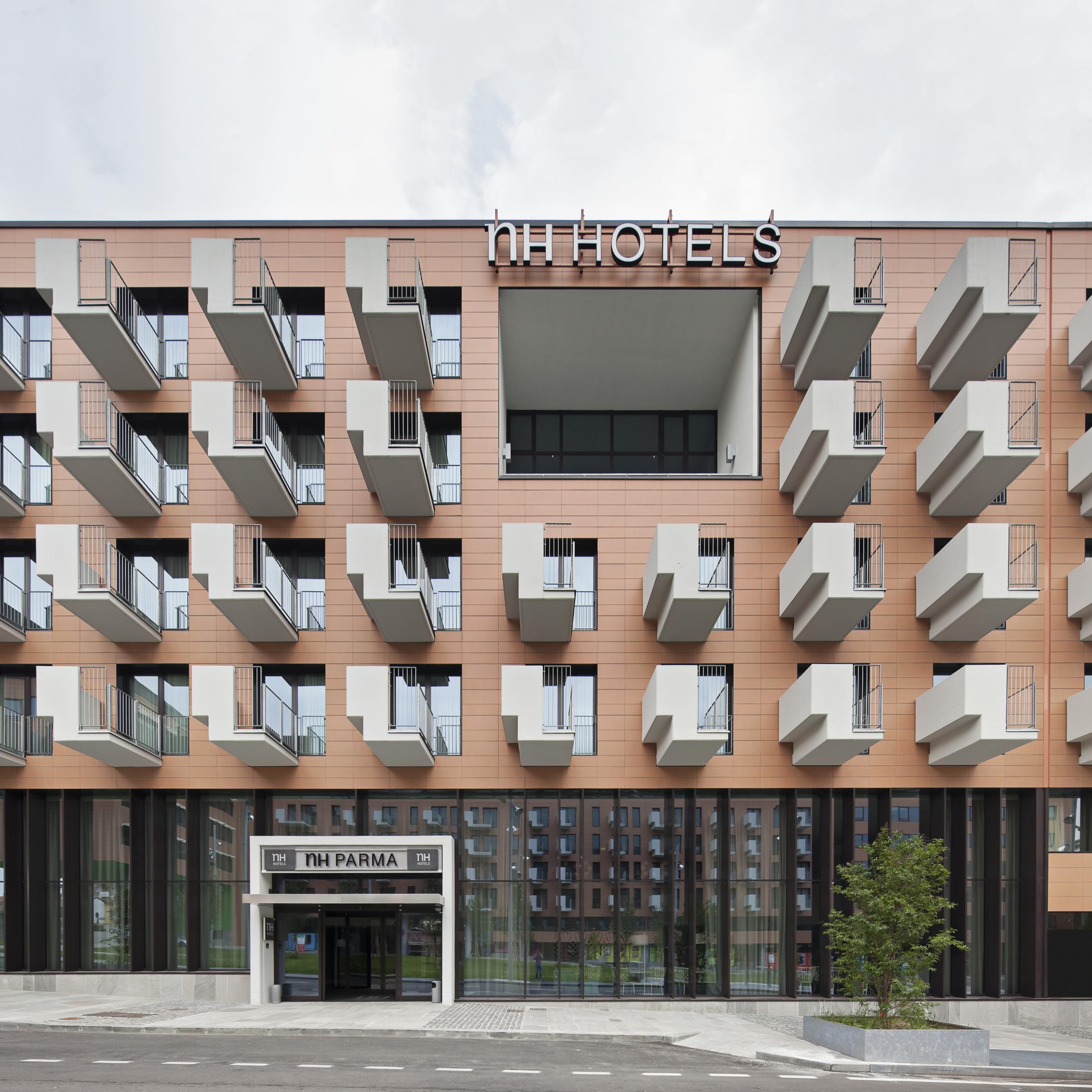A modern hotel building with multiple balconies and a clear entrance labeled "NH PARMA".