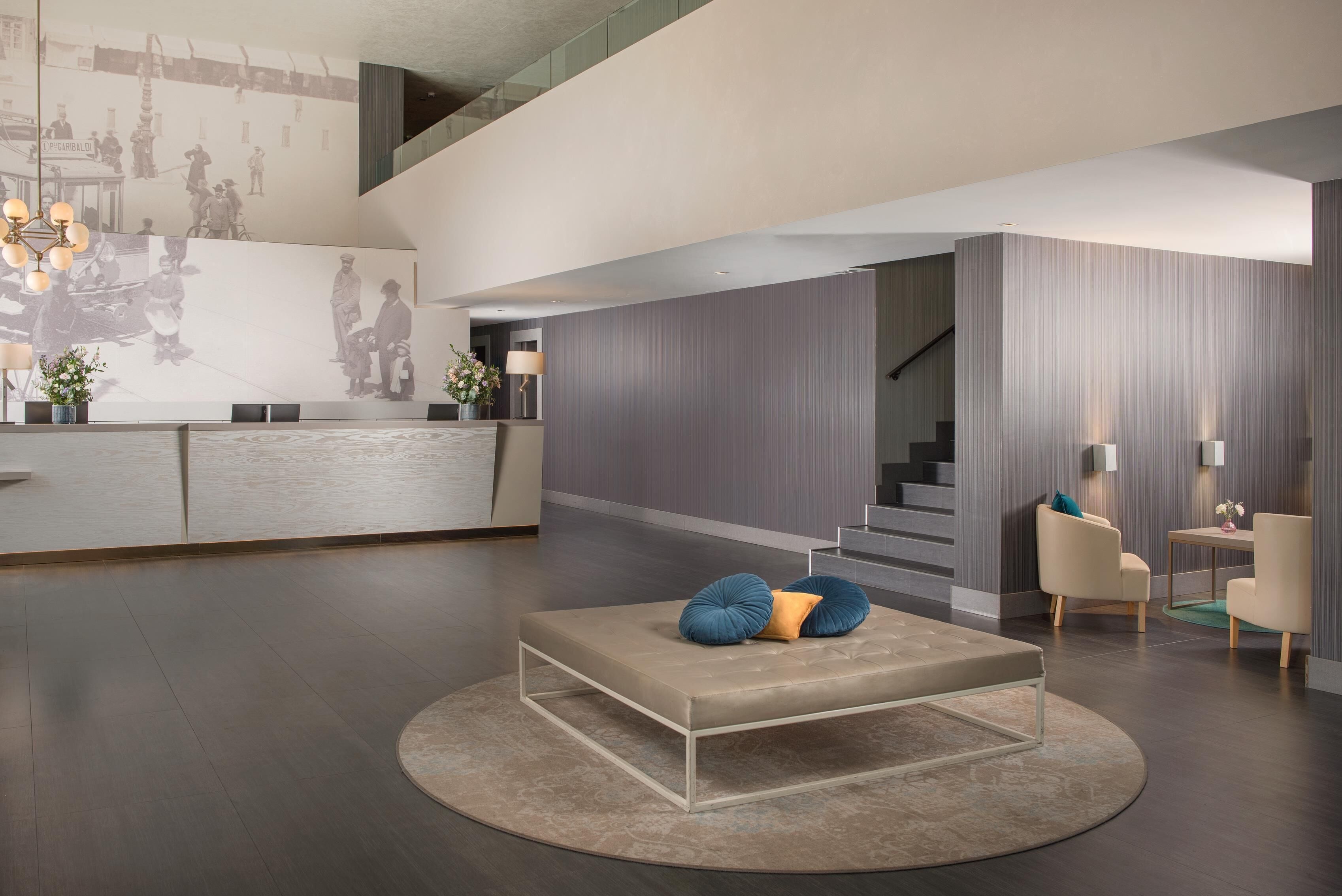 Um lobby moderno com balcão de recepção, escada e área de estar com sofá e cadeiras.