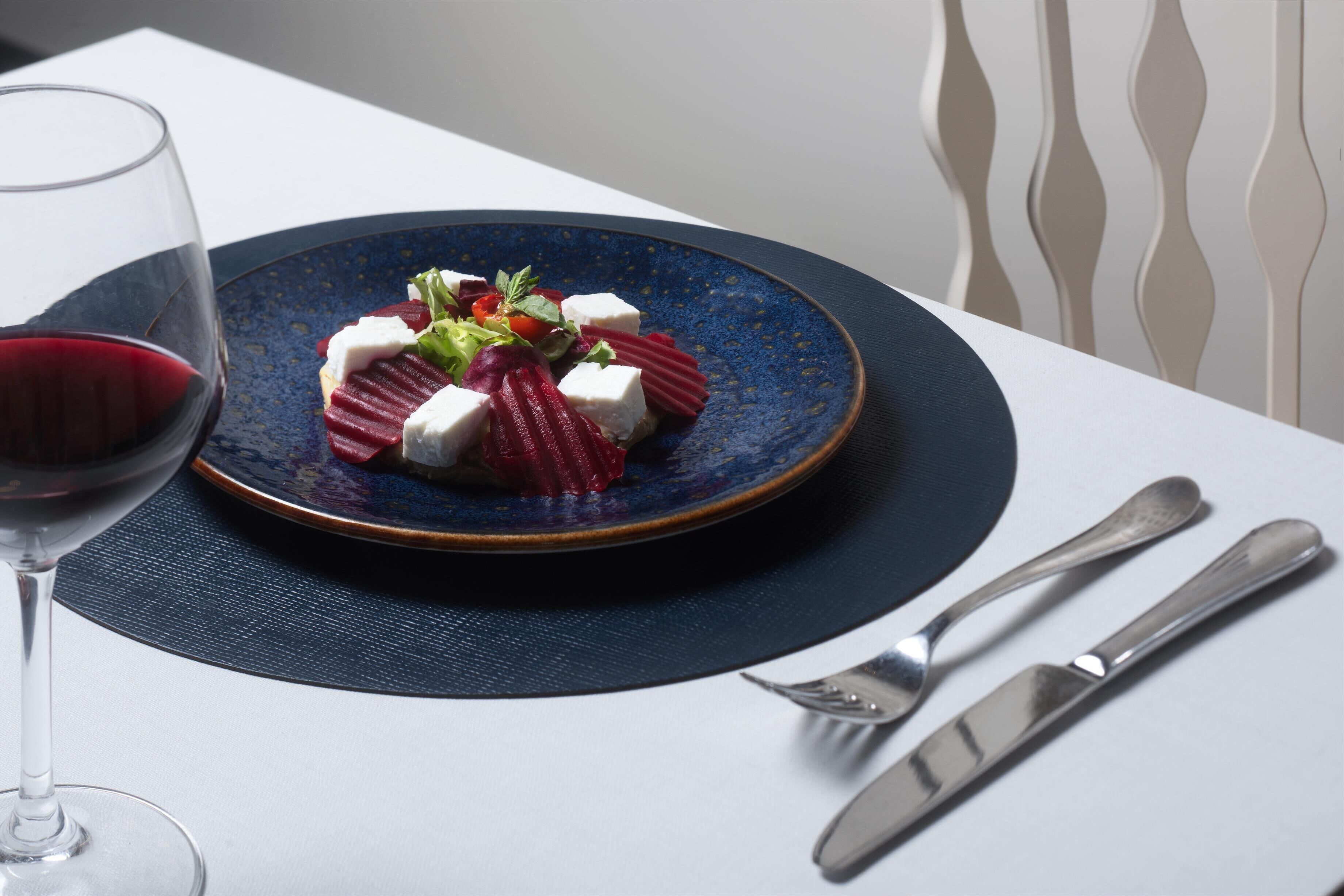 Un plato azul con una ensalada sobre un mantel blanco.