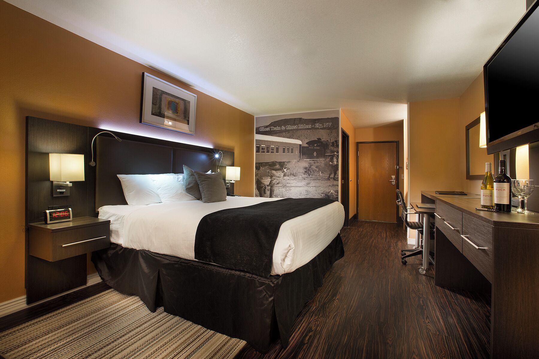 A hotel room with a large bed, a desk with a chair, a television, and a wall-mounted picture.
