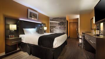 A hotel room with a large bed, a desk with a chair, a television, and a wall-mounted picture.