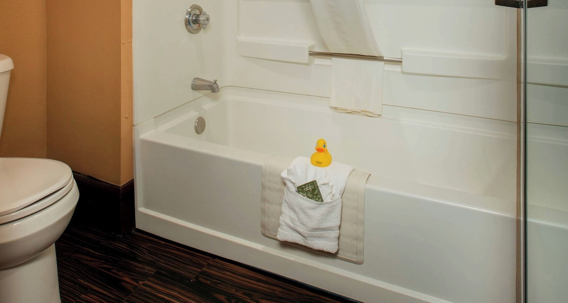 A bathroom with a white bathtub, a toilet, and a wooden floor.