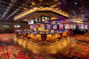 A bar area with multiple gaming machines, a large screen displaying sports, and a bar counter with stools. - Prospector Hotel & Gambling Hall (Ely)