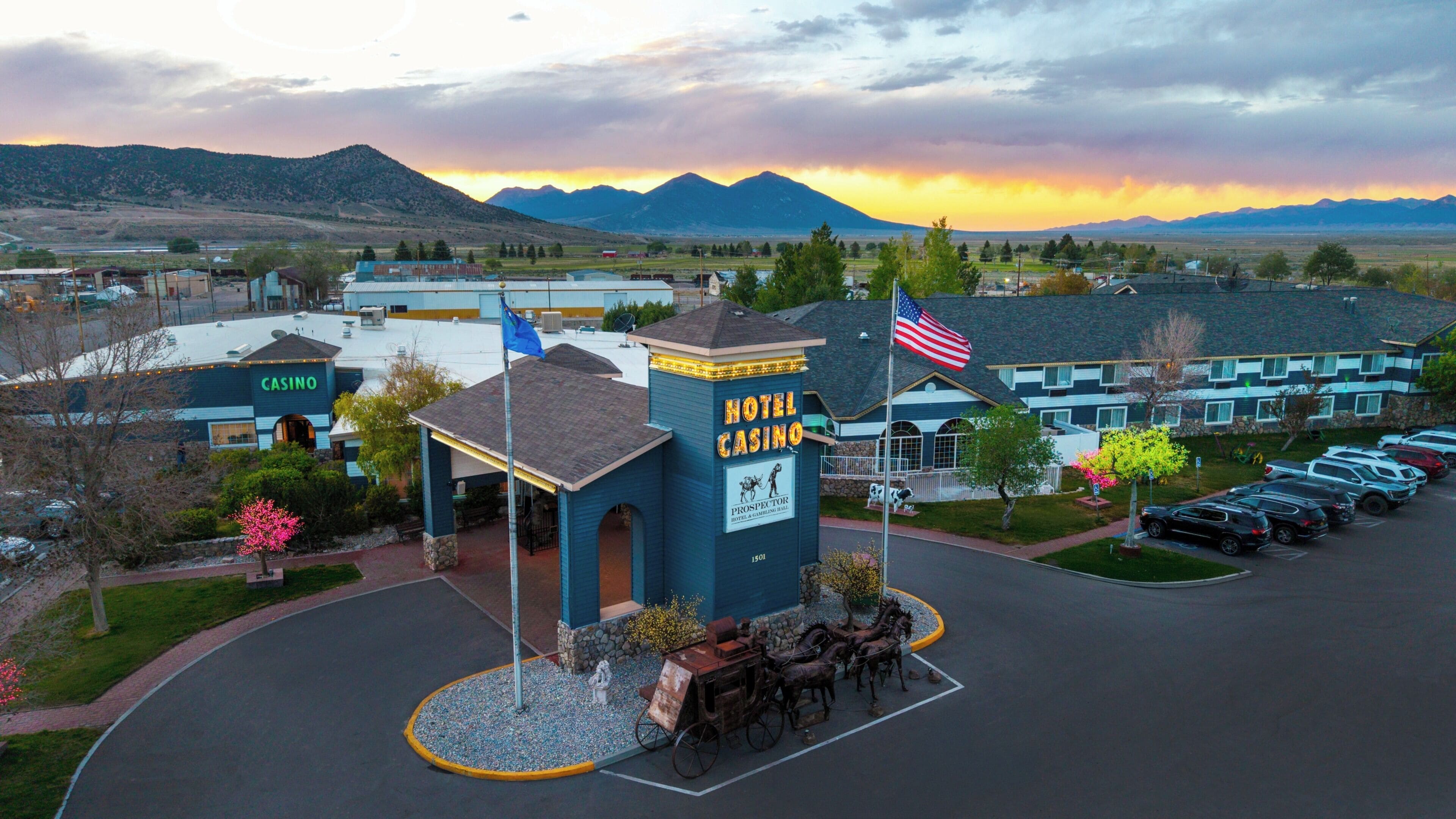 A hotel with a prominent casino sign, a flagpole with an American flag, and a parking lot with cars.