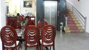 A hotel lobby with a reception desk, a dining area with wooden chairs, a flower vase, and a sign indicating karaoke and massage services. - Thanh Hong Hotel (Ho Chi Minh City)