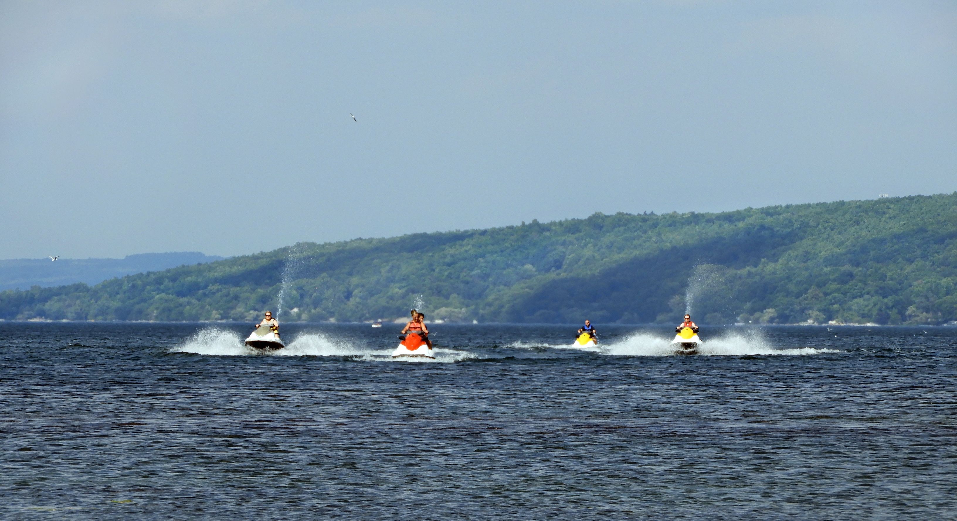 Three jet skis on a body of water with a forested hill in the background.