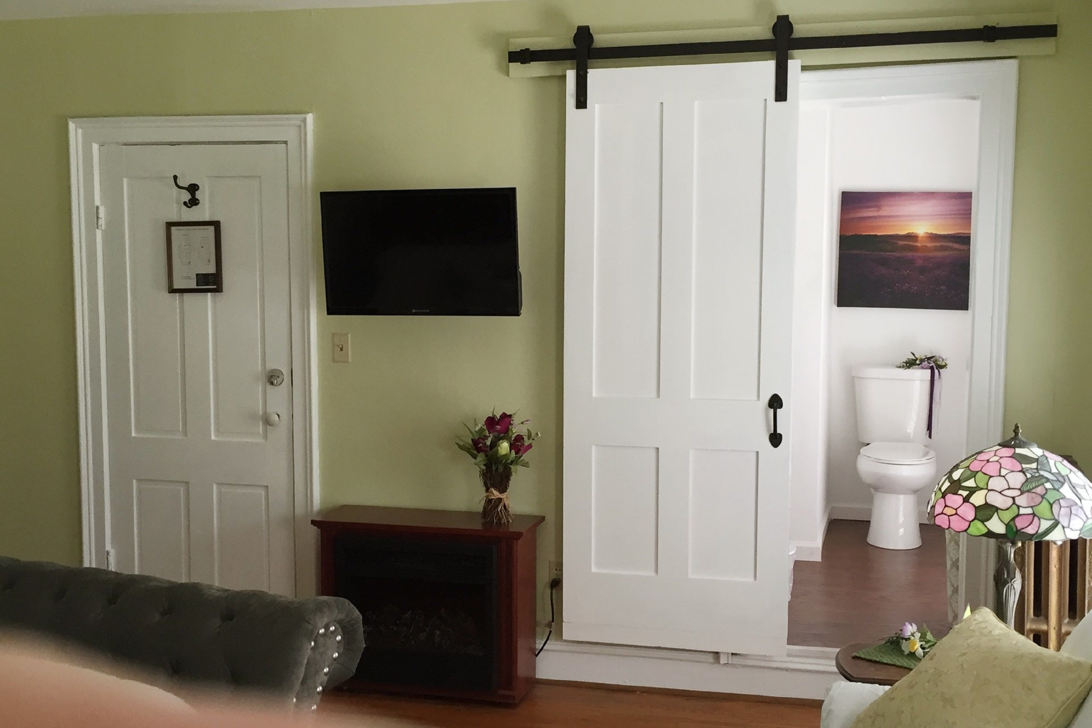 A room with a sliding door, a fireplace, a television mounted on the wall, and a framed picture above the toilet.