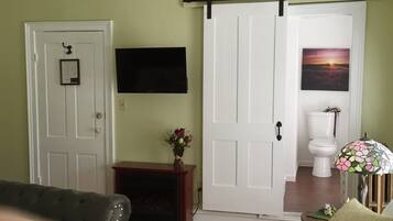 A room with a sliding door, a fireplace, a television mounted on the wall, and a framed picture above the toilet.