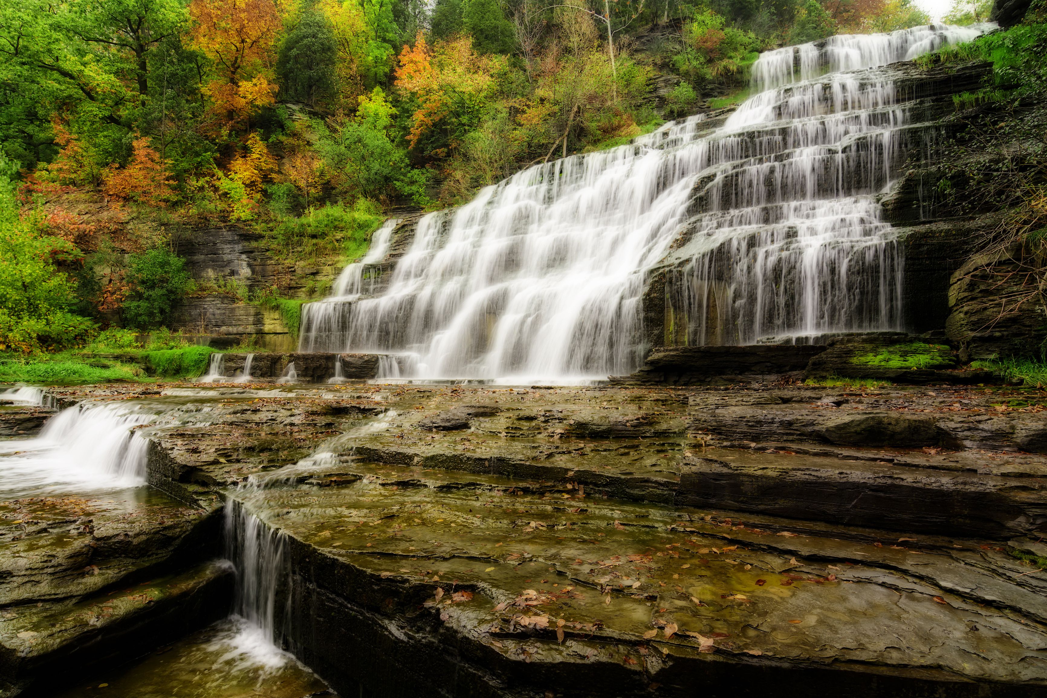 Une cascade à plusieurs niveaux, entourée d'un feuillage automnal.