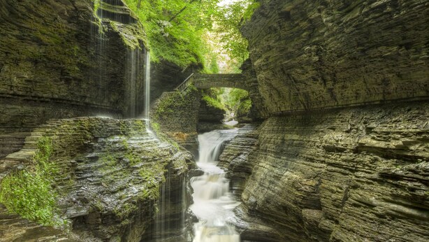 Un canyon étroit avec une cascade et un pont de pierre.