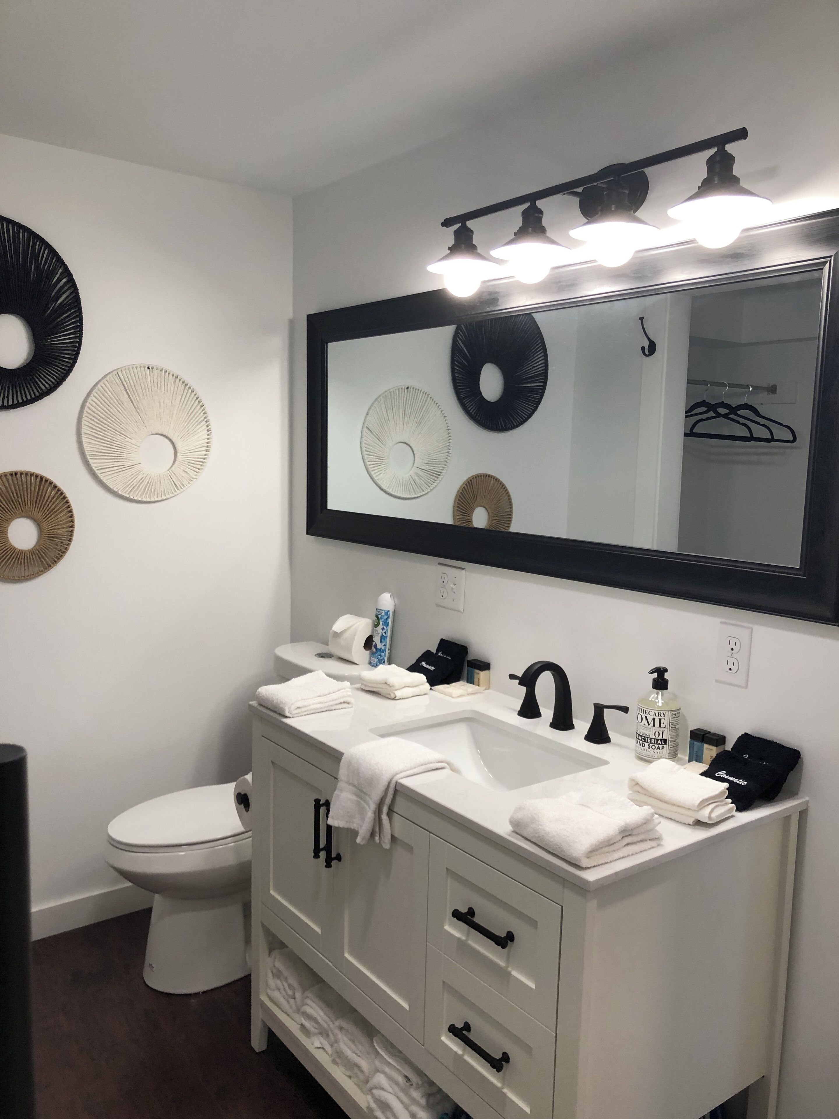 Uma casa de banho moderna com toucador branco, espelho grande e elementos decorativos nas paredes.