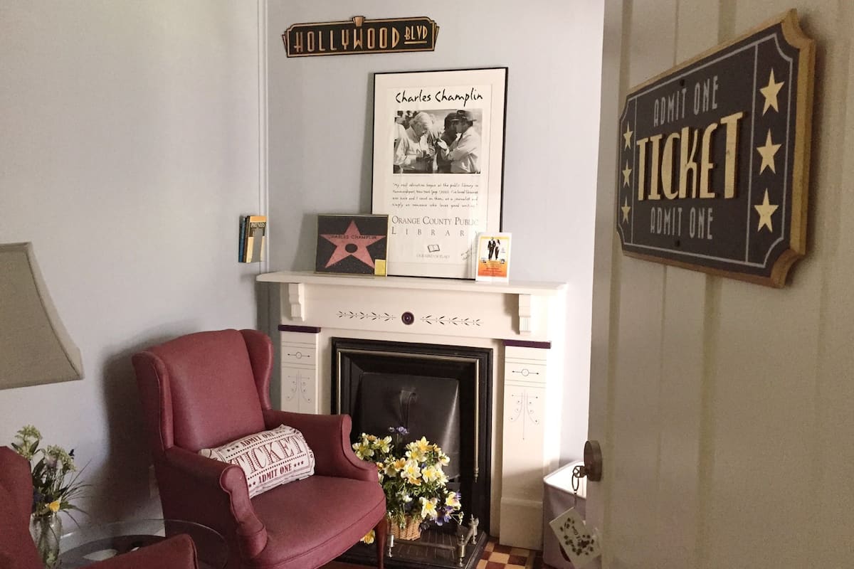 Un salón con un sillón rojo, una chimenea y un cartel enmarcado de Charles Chaplin.