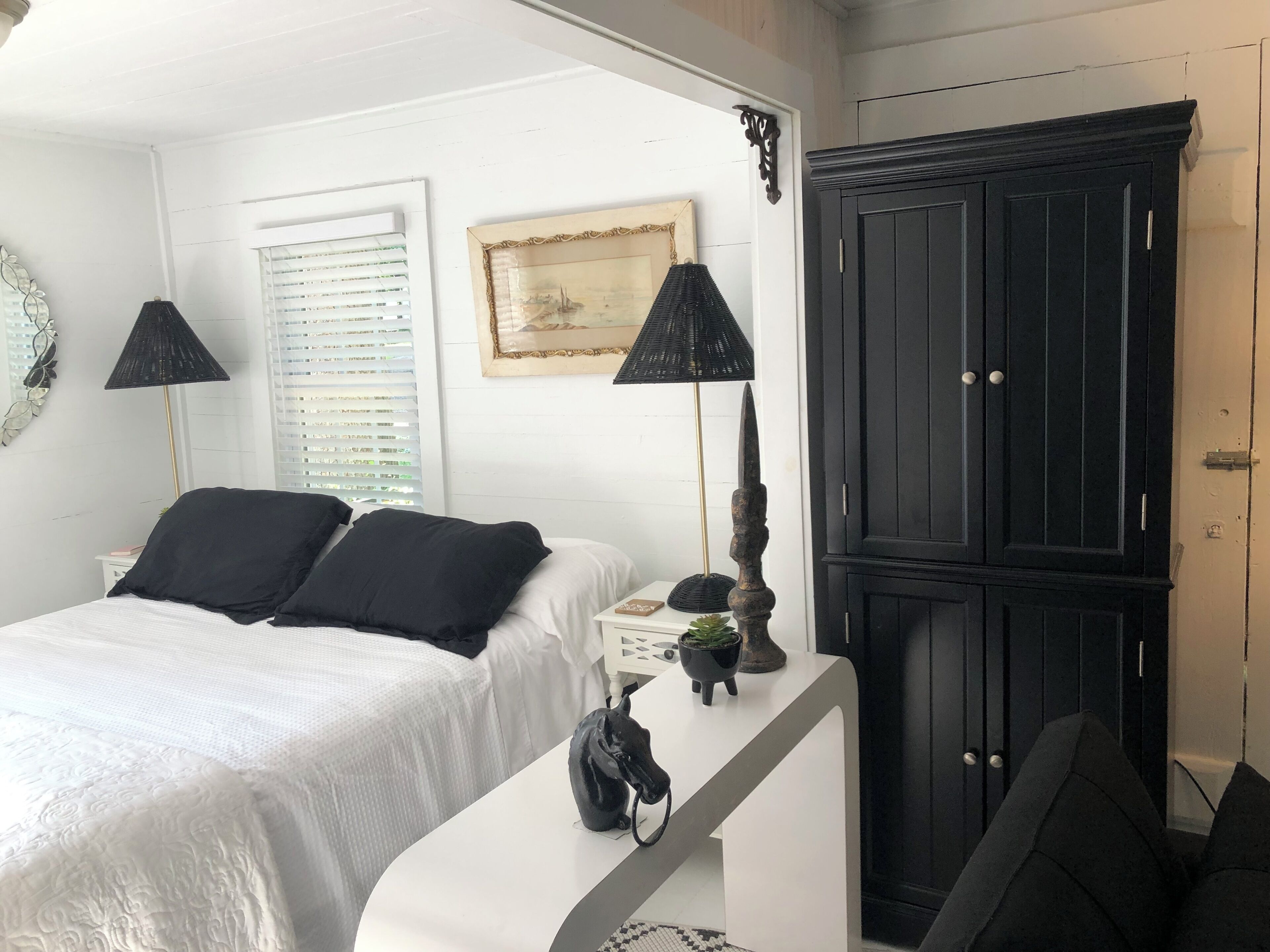 A bedroom with a bed, two black lamps, a black wardrobe, and a framed picture on the wall.
