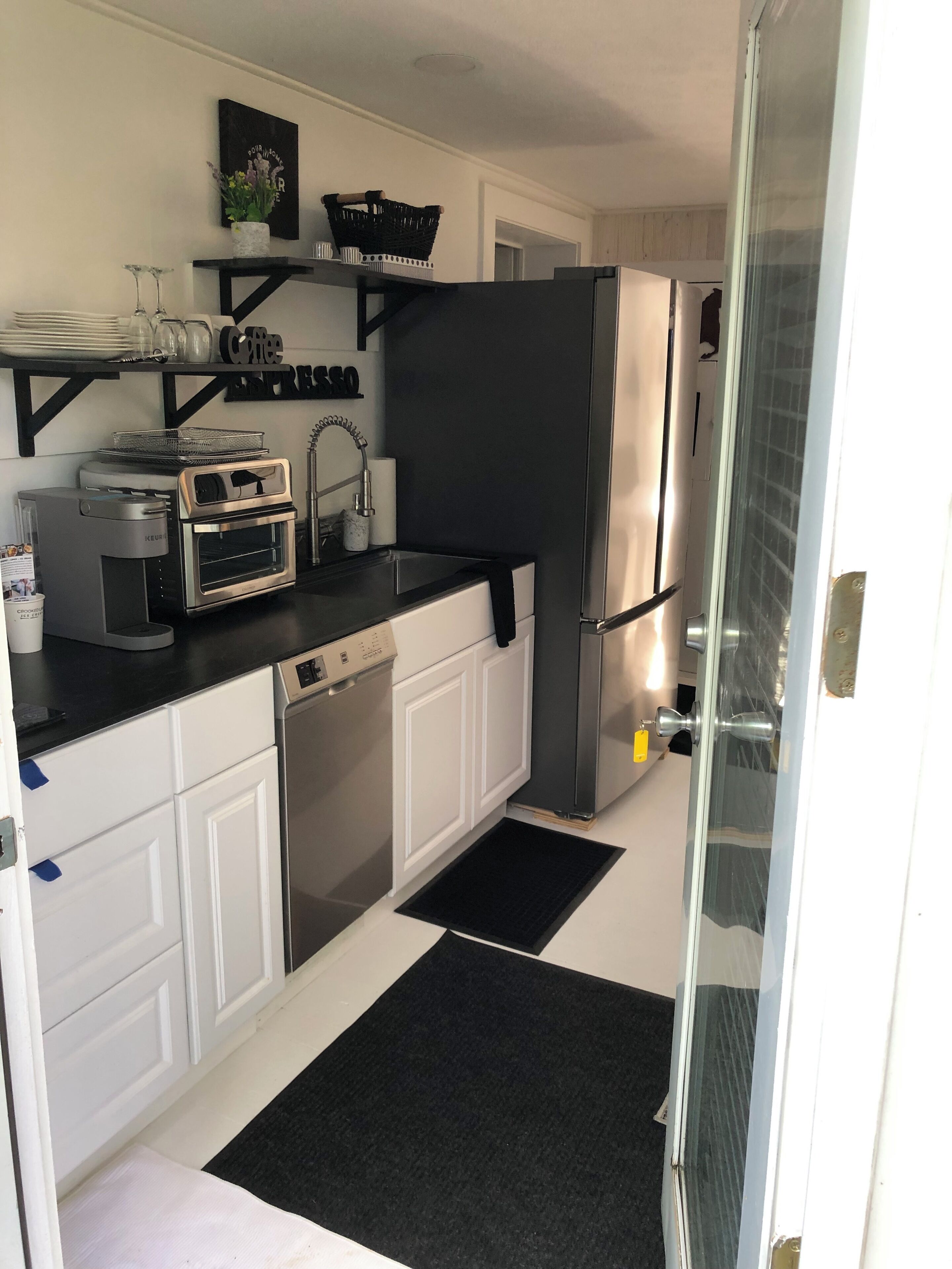 A compact kitchen with white cabinets, a black countertop, a stainless steel refrigerator, a coffee machine, and a small oven.