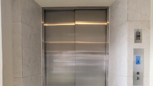 A modern elevator with a metallic finish, control panel with buttons, and a marble-tiled wall.