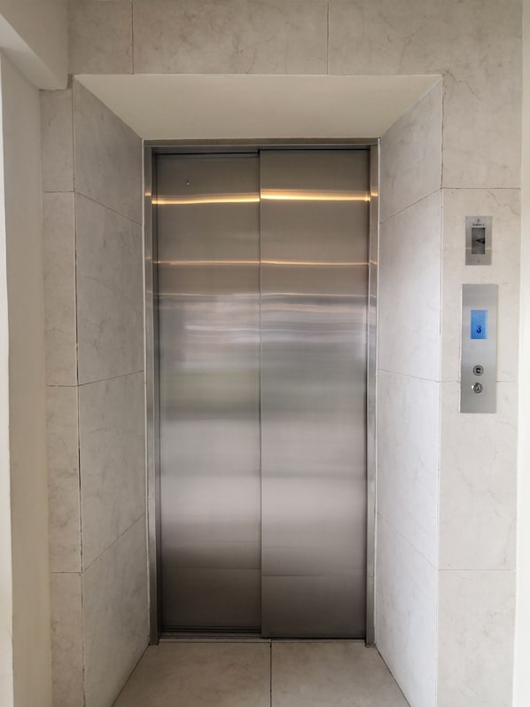 Un ascenseur moderne avec une finition métallique, un panneau de commande doté de boutons et un mur recouvert de carreaux de marbre.