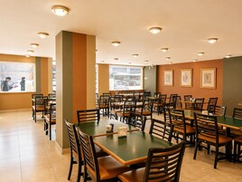 Un comedor con varias mesas y sillas, ventanas amplias con persianas y obras de arte enmarcadas en las paredes.