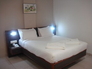 A neatly made bed with white linens, a bedside table with a phone, and a wall-mounted painting. - Beith Hotel (Kanayannur)