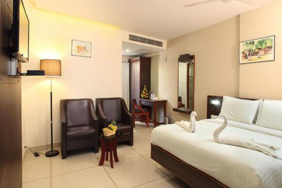 A hotel room with a bed, two armchairs, a small table, a lamp, a ceiling fan, and a TV.