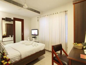 A hotel room with a bed, a television, a desk with a chair, and a window with curtains. - Beith Hotel (Kanayannur)