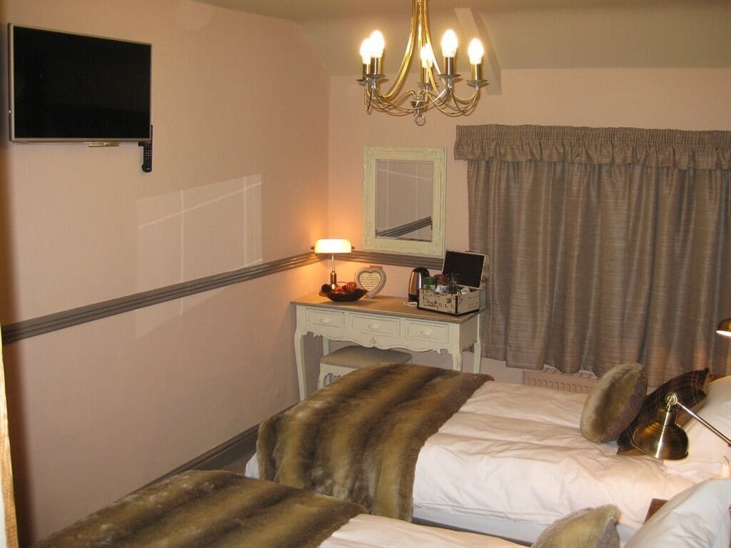 A hotel room with a bed, a desk with a lamp, a television, and a chandelier.