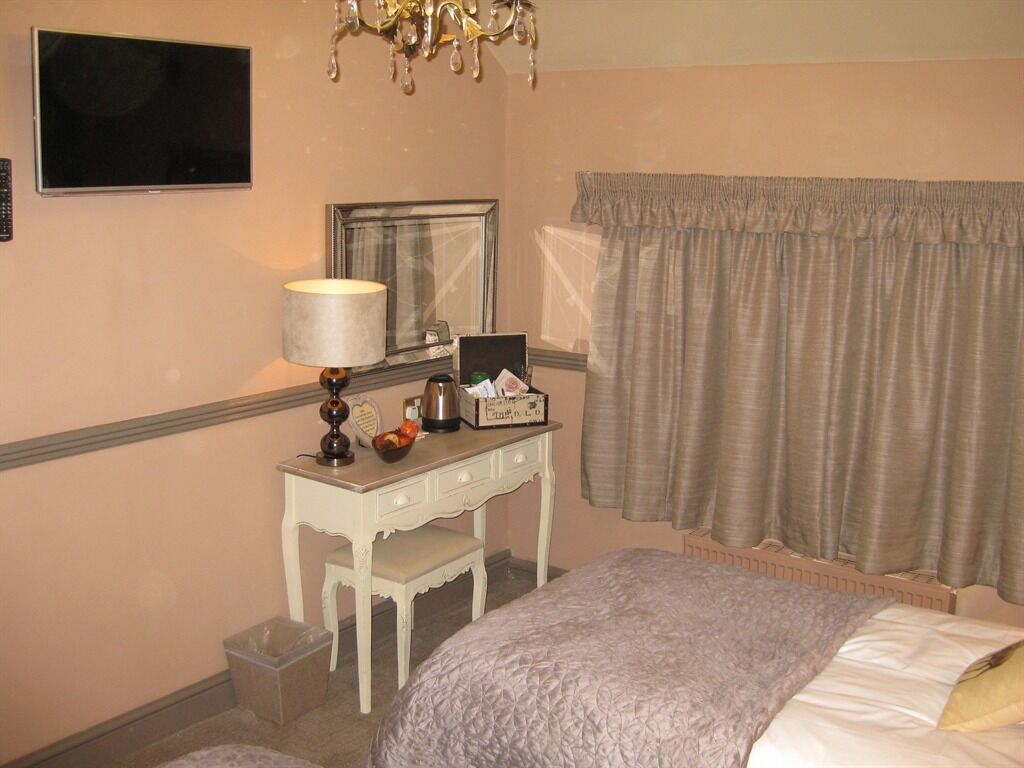 A hotel room with a bed, a desk with a lamp, a mirror, a television, and a window with curtains.