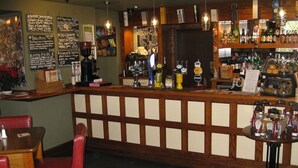 Eine Bar mit Holztresen, Barhocker und einer Auswahl an Flaschen und Gläsern.