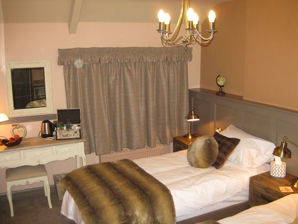 Una habitación de hotel con cama, escritorio, silla, cómoda, mesita de noche, lámpara, candelabro y ventana con cortinas.