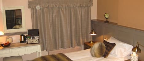 Una habitación de hotel con cama, escritorio, silla, cómoda, mesita de noche, lámpara, candelabro y ventana con cortinas.