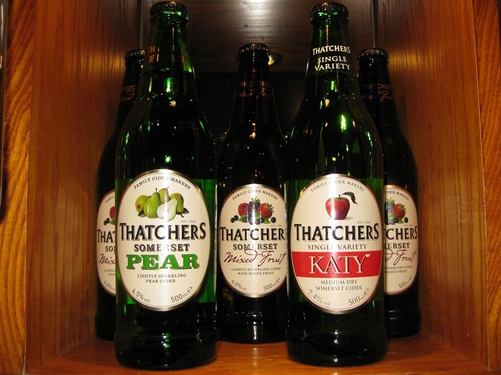Four bottles of Thatchers Somerset Pear cider in a wooden cabinet.