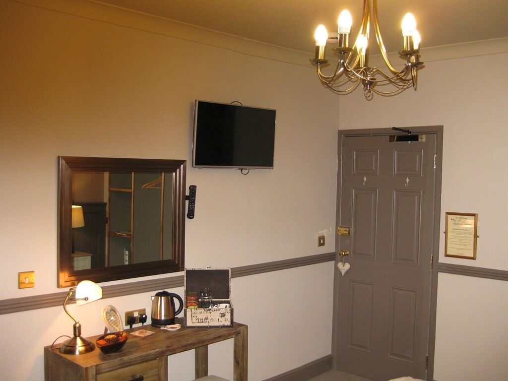 A hotel room with a wooden desk, a television mounted on the wall, a chandelier, and a door with a plaque.