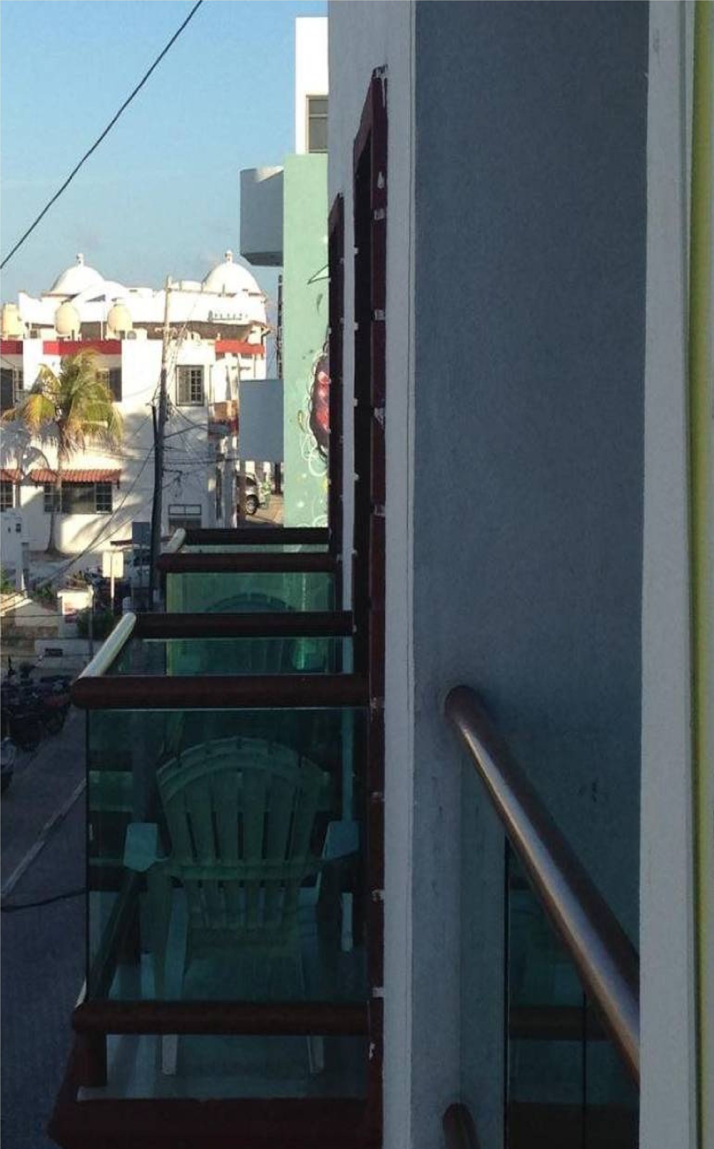 A balcony with a metal railing overlooking a street with buildings and a parked car.