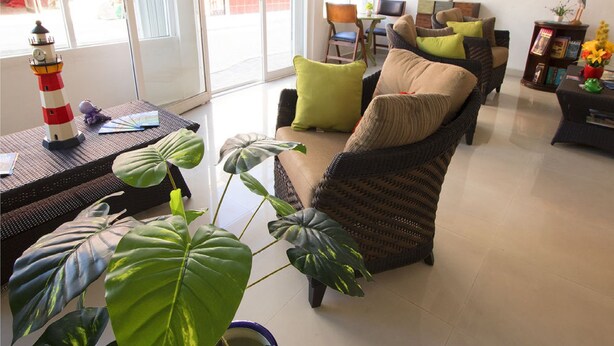 A spacious living room with a large window, wicker furniture, and a bookshelf. - Hotel Isleño (Isla Mujeres)