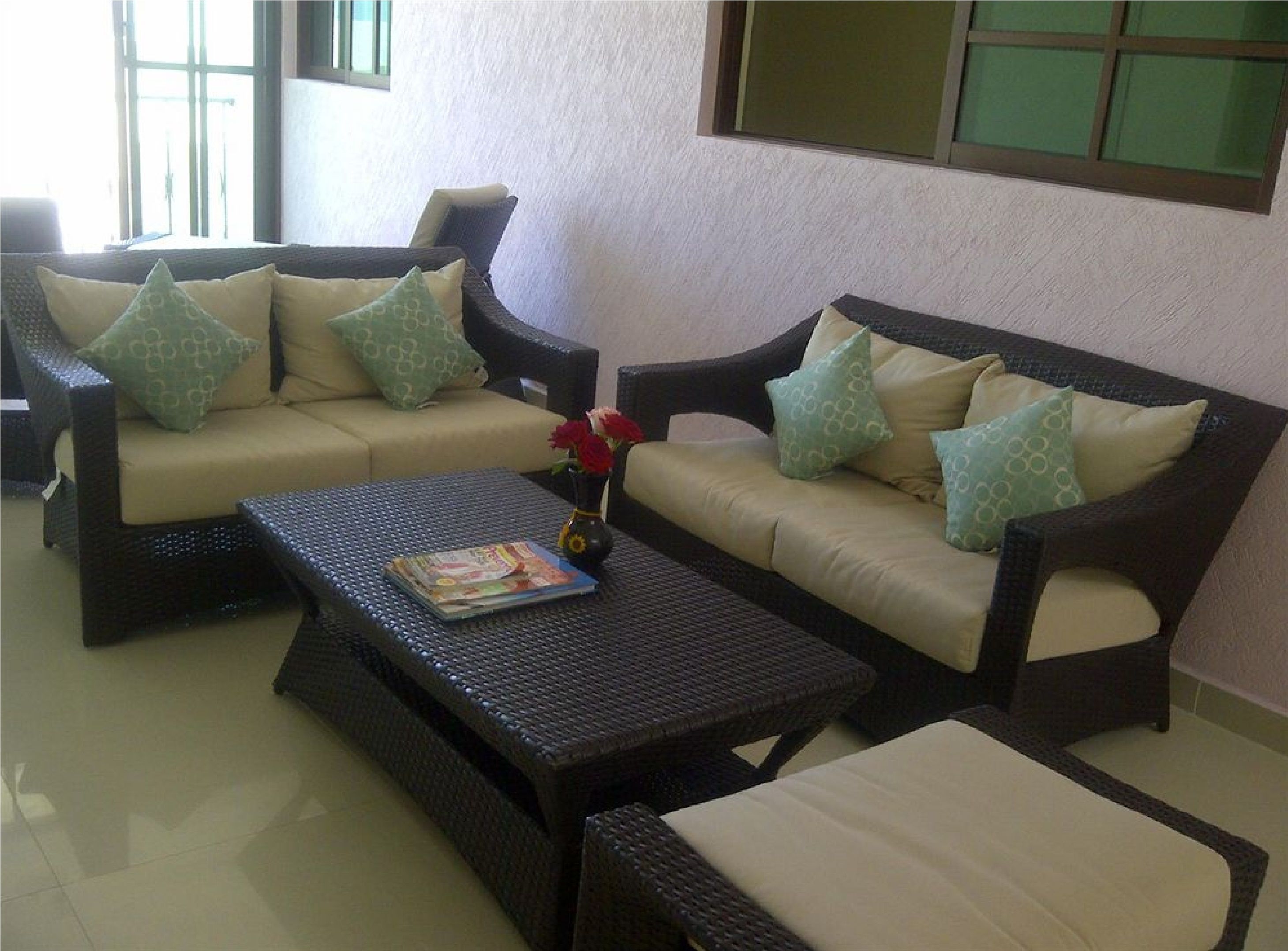 A furnished outdoor seating area with two sofas and a coffee table, featuring patterned cushions and a vase with flowers.