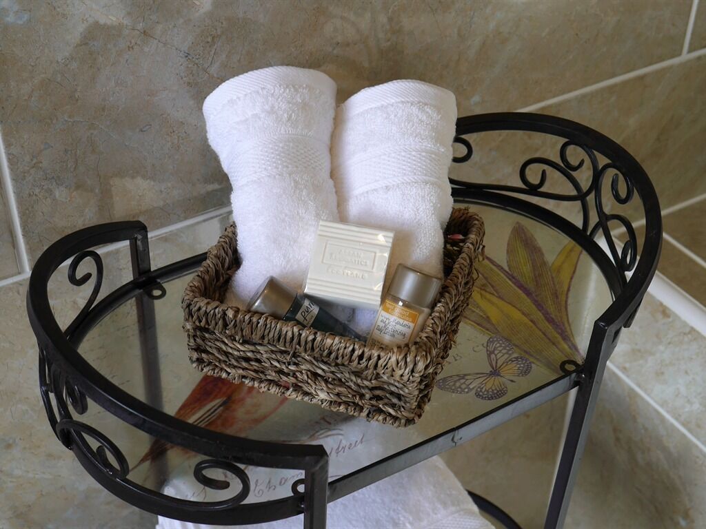 A glass table with a wicker basket containing two white towels, a bar of soap, and a bottle of lotion.