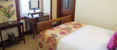 A bedroom with a bed, a desk, a chair, a mirror, and a window with blinds.