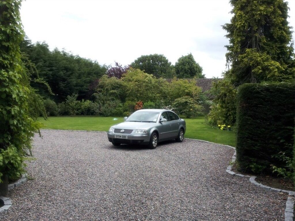 A silver sedan parked on a gravel driveway surrounded by lush greenery and hedges.