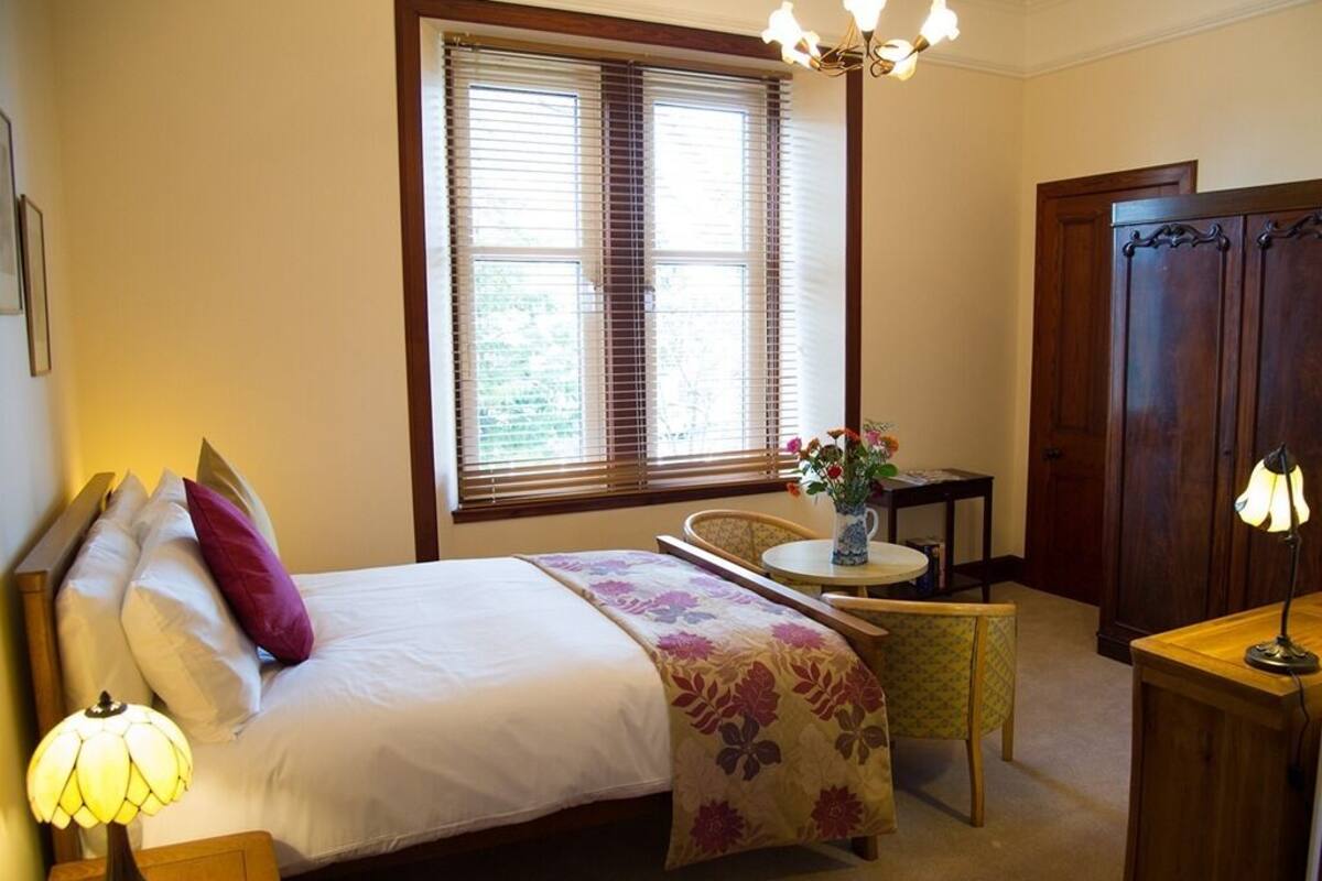 Quarto com cama, mesa de cabeceira, cadeira, mesinha redonda e guarda-roupa de madeira.