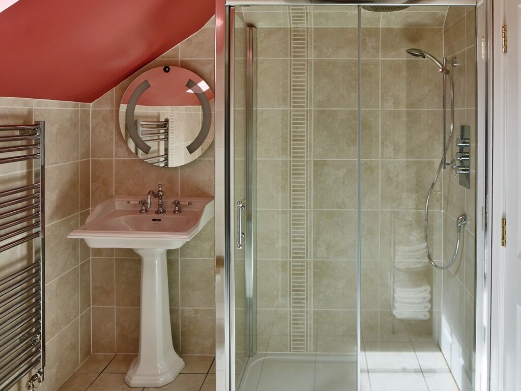 A bathroom with a pedestal sink, a glass-enclosed shower, and a mirror with a circular frame.