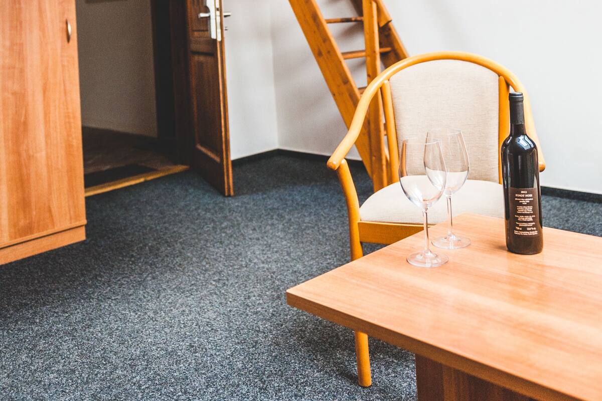 A room with a wooden staircase, a chair, a table with a bottle and glasses, and a door leading to another room.